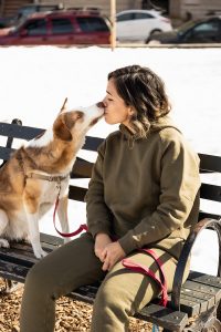 woman in gray coat sitting on black chair beside brown and white dog during daytime